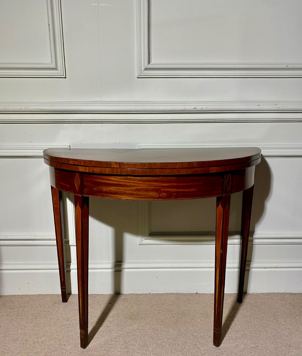 An 18th-century Sheraton mahogany demi-lune tea table with line inlay and tapered square legs against a white wall. View II