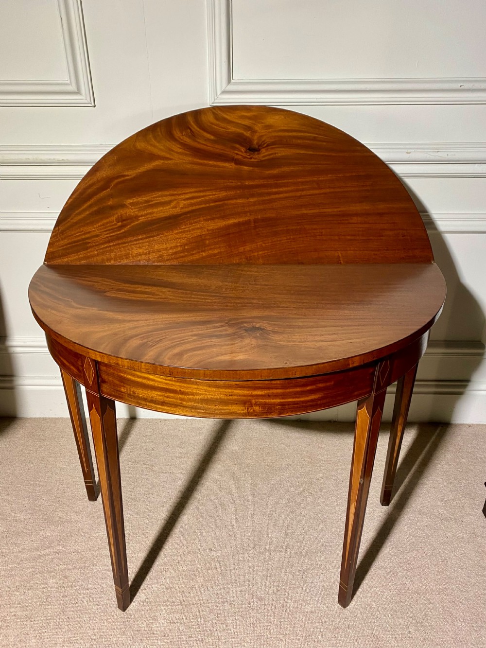An 18th-century Sheraton mahogany demi-lune tea table with line inlay and tapered square legs against a white wall. View VI