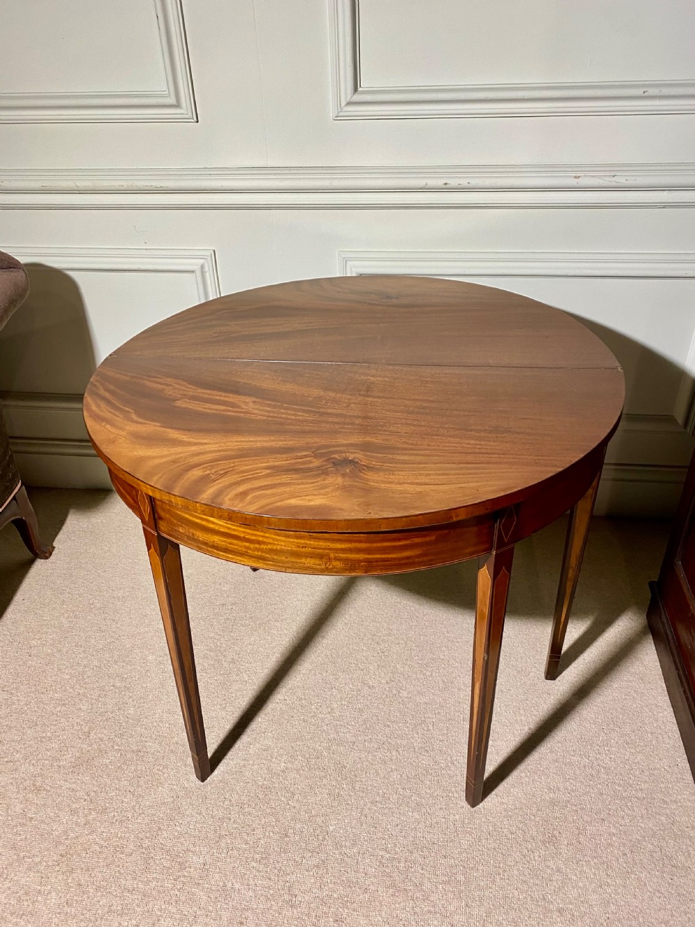 An 18th-century Sheraton mahogany demi-lune tea table with line inlay and tapered square legs against a white wall. View VIII