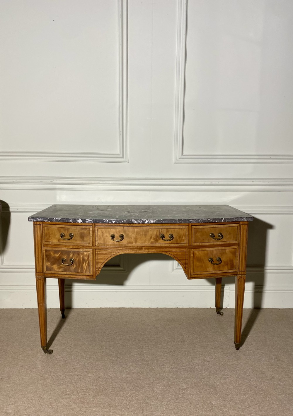 A 19th-century satinwood dressing table featuring a grey marble top, five drawers with brass drop handles, a central arch, and tapered legs on castors. View II