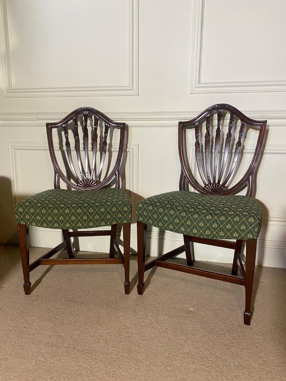 A pair of mahogany Hepplewhite style side chairs featuring carved shield backs and green patterned upholstered seats.