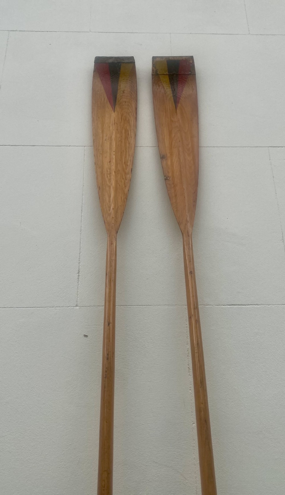 A pair of long antique wooden rowing oars with painted geometric triangular motifs in yellow, black, and red at the blades.