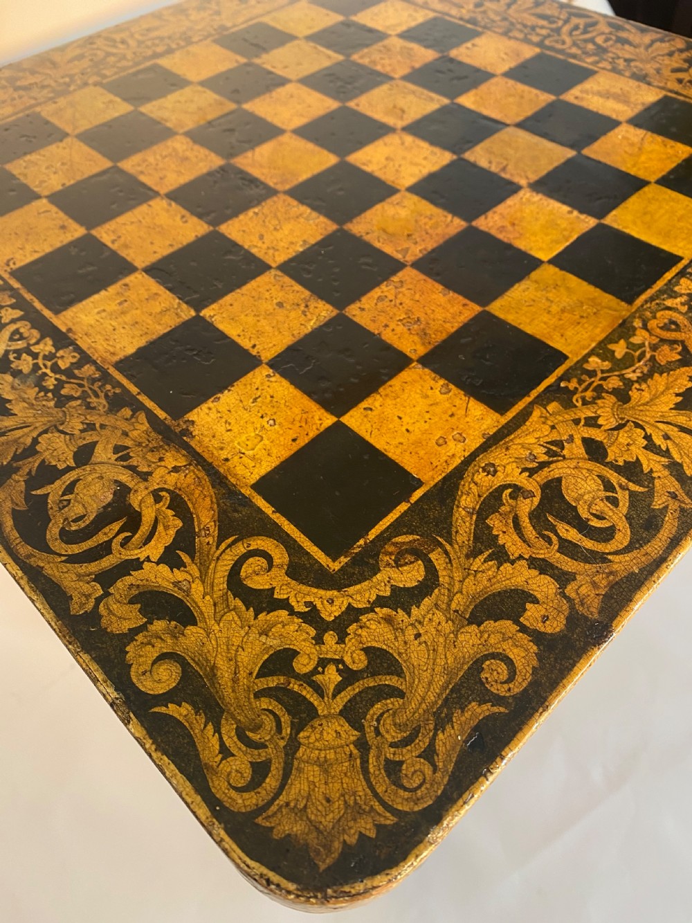 A square Regency ebonised chess table featuring detailed foliate penwork framing a central chessboard top, supported by a turned central pedestal and tripod base. View III