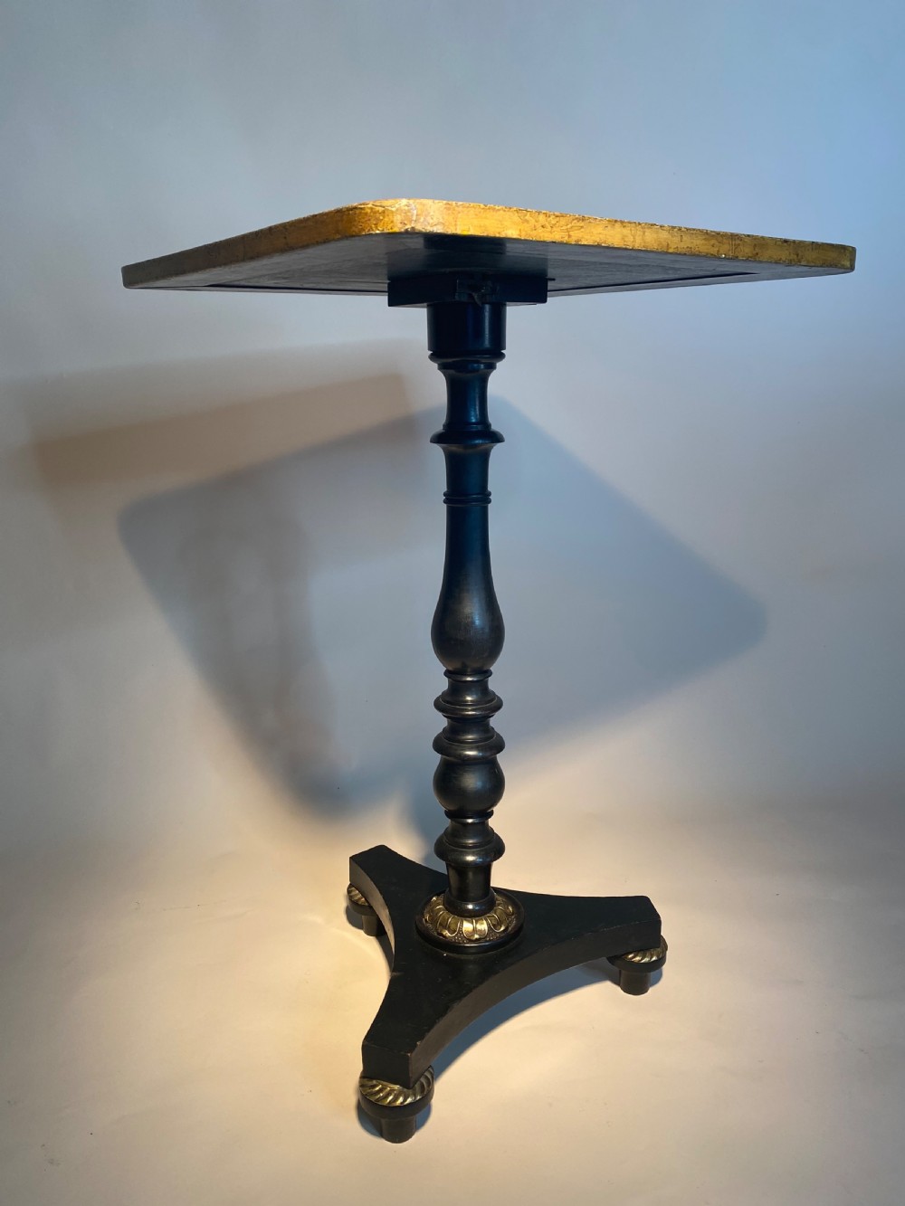 A square Regency ebonised chess table featuring detailed foliate penwork framing a central chessboard top, supported by a turned central pedestal and tripod base. View VII