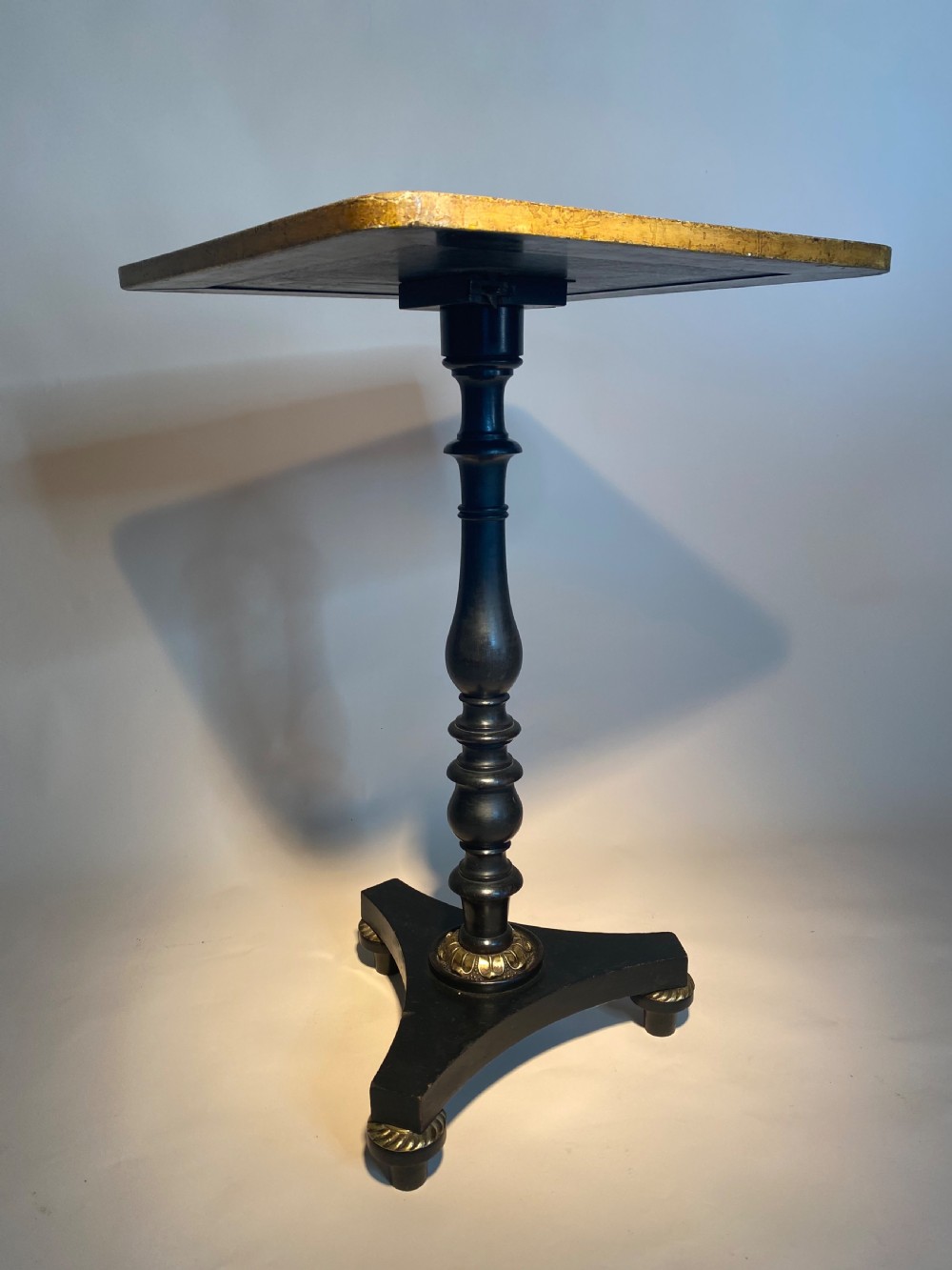 A square Regency ebonised chess table featuring detailed foliate penwork framing a central chessboard top, supported by a turned central pedestal and tripod base. View XII