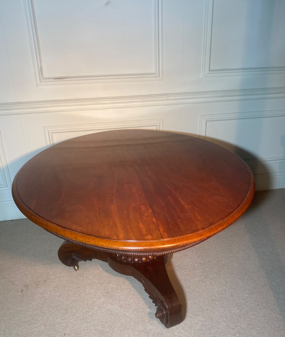 An antique Regency mahogany oval breakfast table featuring a carved fluted pedestal support and scroll feet with brass castors. View III
