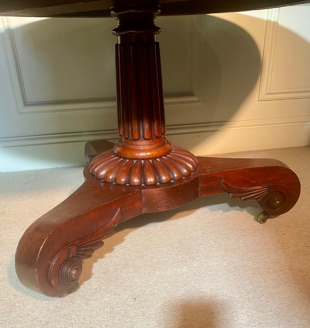 An antique Regency mahogany oval breakfast table featuring a carved fluted pedestal support and scroll feet with brass castors. View VIII