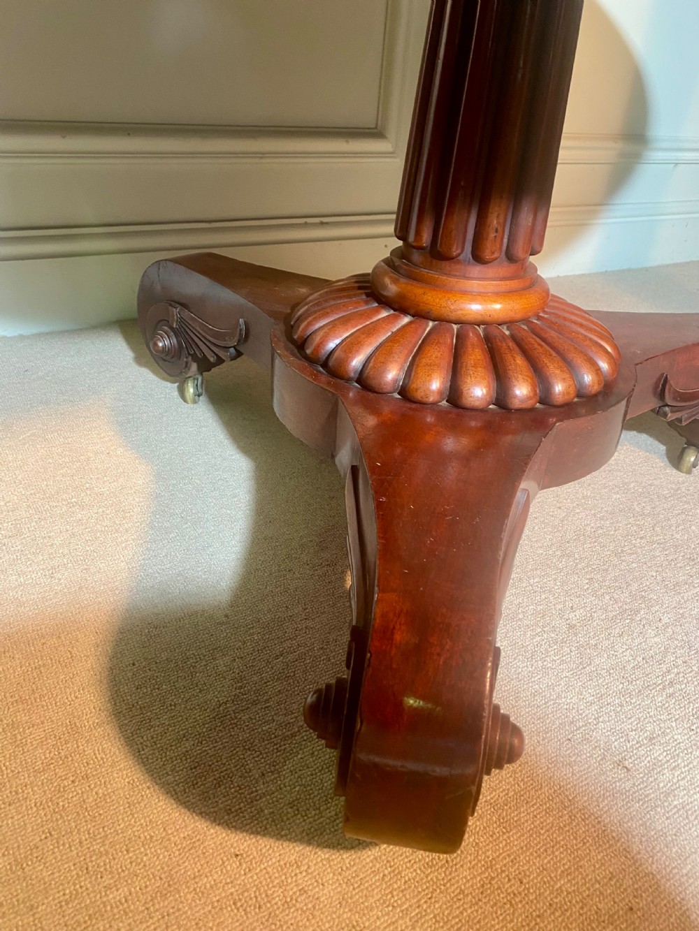 An antique Regency mahogany oval breakfast table featuring a carved fluted pedestal support and scroll feet with brass castors. View IX