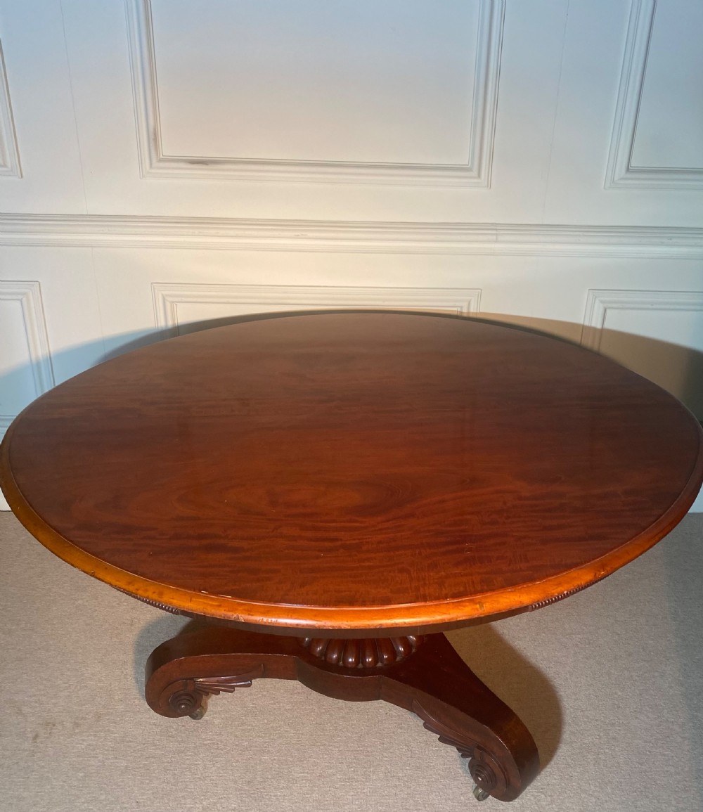 An antique Regency mahogany oval breakfast table featuring a carved fluted pedestal support and scroll feet with brass castors. View XI