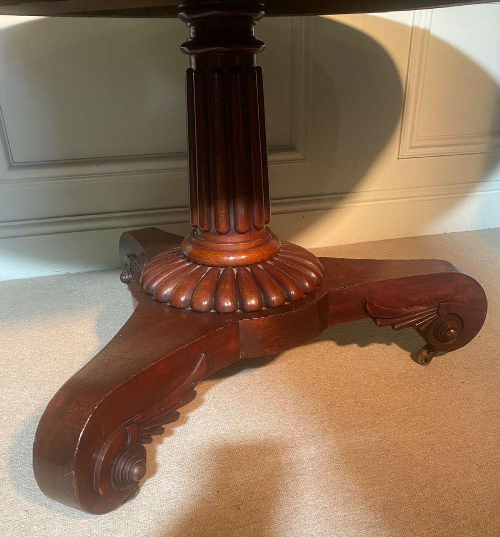 An antique Regency mahogany oval breakfast table featuring a carved fluted pedestal support and scroll feet with brass castors. View XII