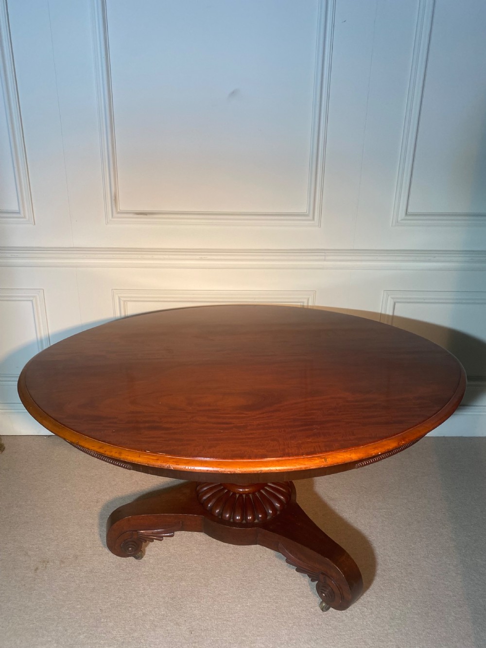 An antique Regency mahogany oval breakfast table featuring a carved fluted pedestal support and scroll feet with brass castors. View XIII