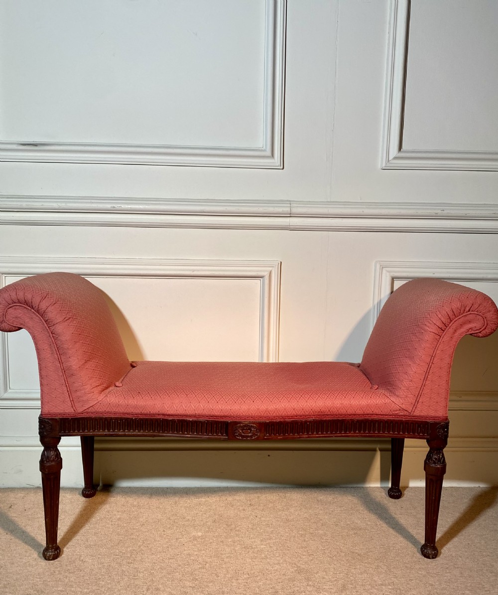 A Hepplewhite style window seat featuring rose pink patterned fabric upholstery, twin scrolled ends, and carved mahogany fluted legs.