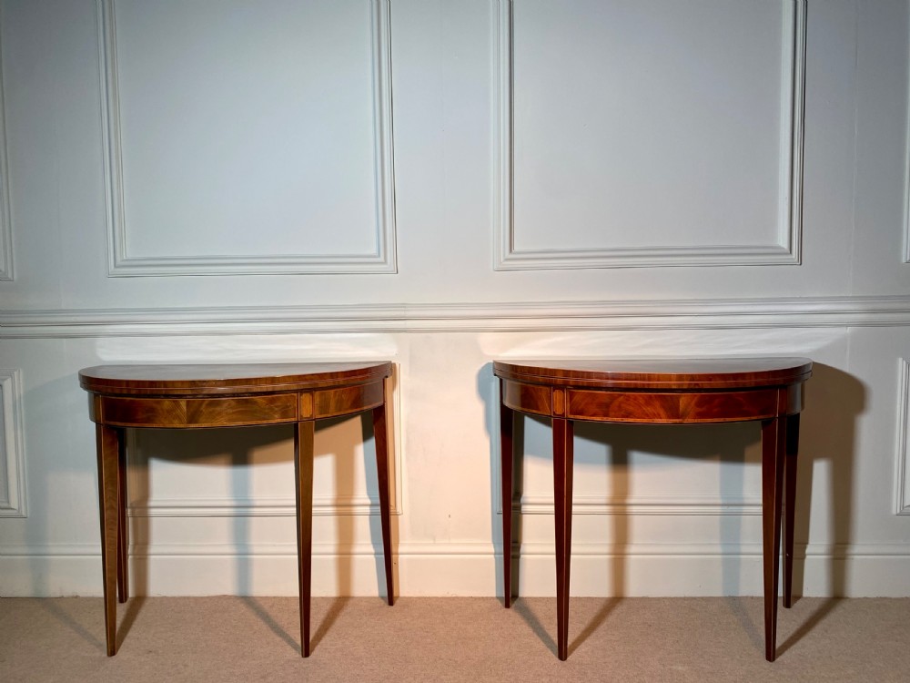 A pair of 18th-century George III mahogany demi-lune card tables with inlaid friezes and square tapered legs positioned against a white panelled wall. View II
