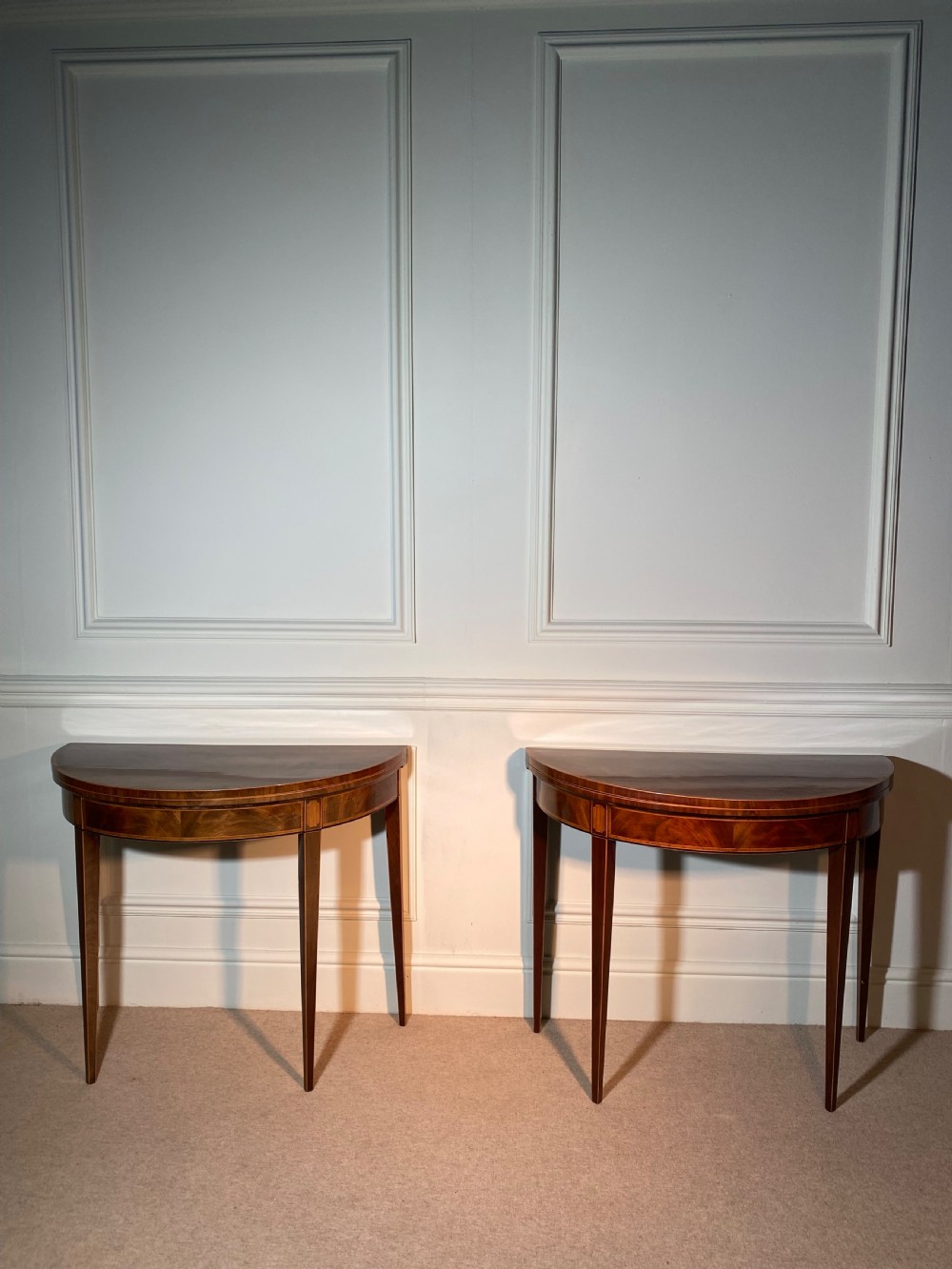 A pair of 18th-century George III mahogany demi-lune card tables with inlaid friezes and square tapered legs positioned against a white panelled wall. View III