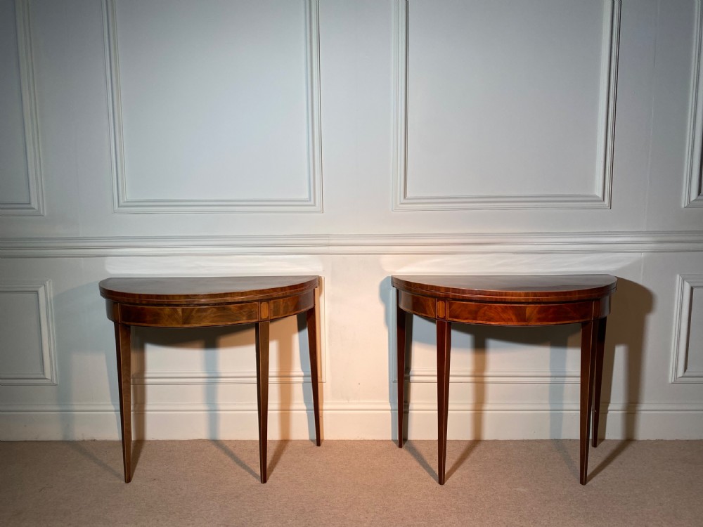 A pair of 18th-century George III mahogany demi-lune card tables with inlaid friezes and square tapered legs positioned against a white panelled wall. View V