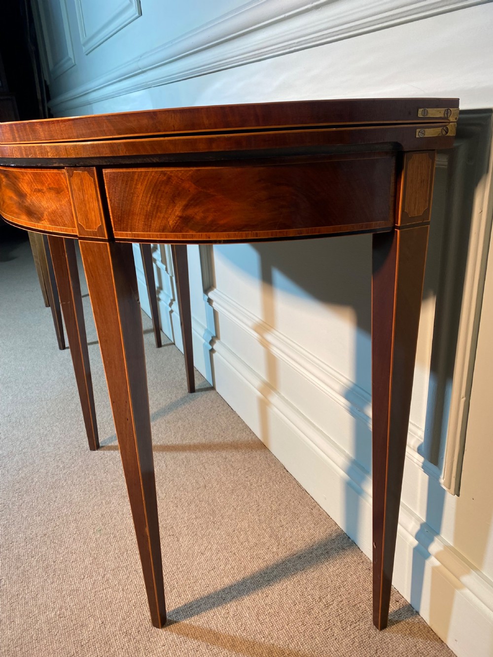 A pair of 18th-century George III mahogany demi-lune card tables with inlaid friezes and square tapered legs positioned against a white panelled wall. View VII