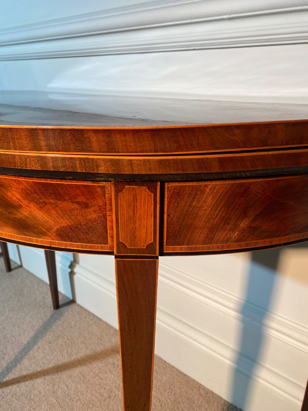 A pair of 18th-century George III mahogany demi-lune card tables with inlaid friezes and square tapered legs positioned against a white panelled wall. View VIII