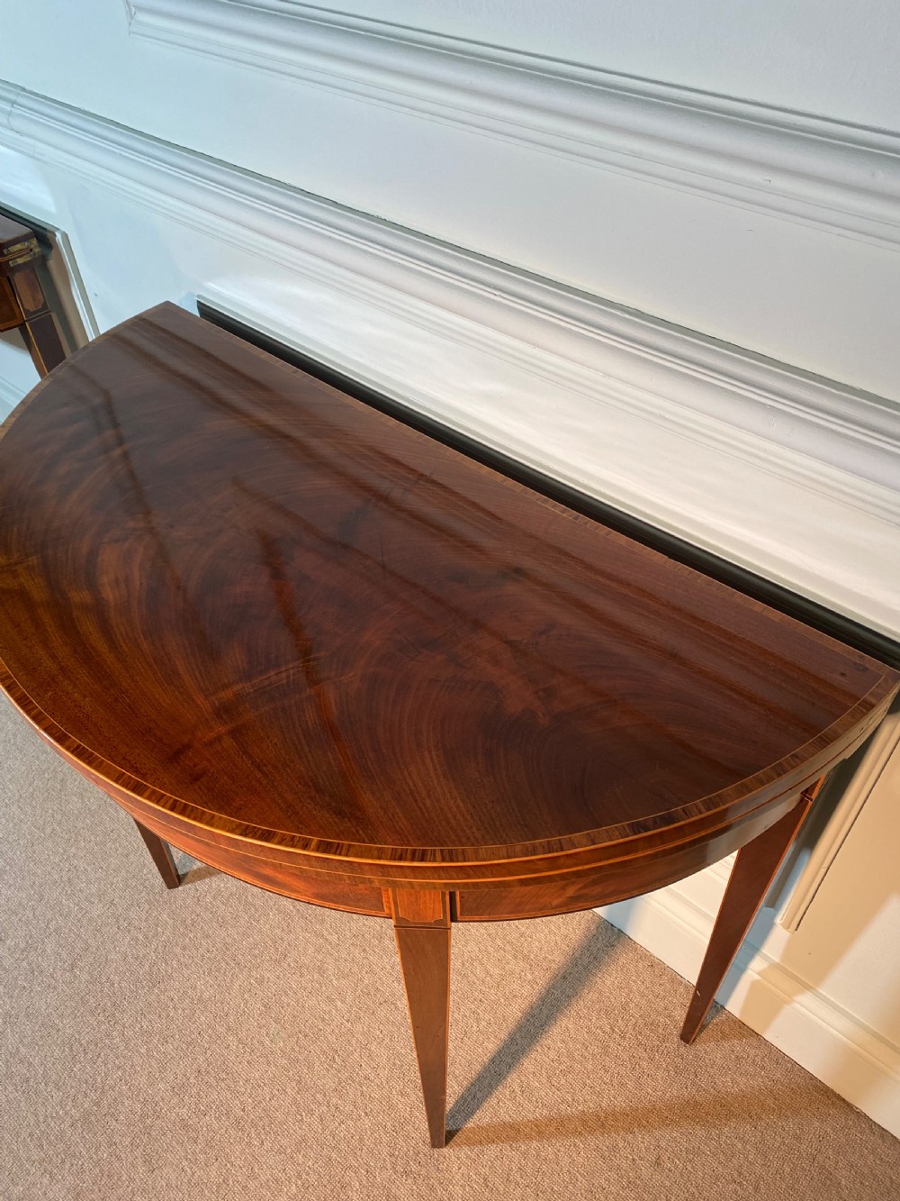 A pair of 18th-century George III mahogany demi-lune card tables with inlaid friezes and square tapered legs positioned against a white panelled wall. View IX