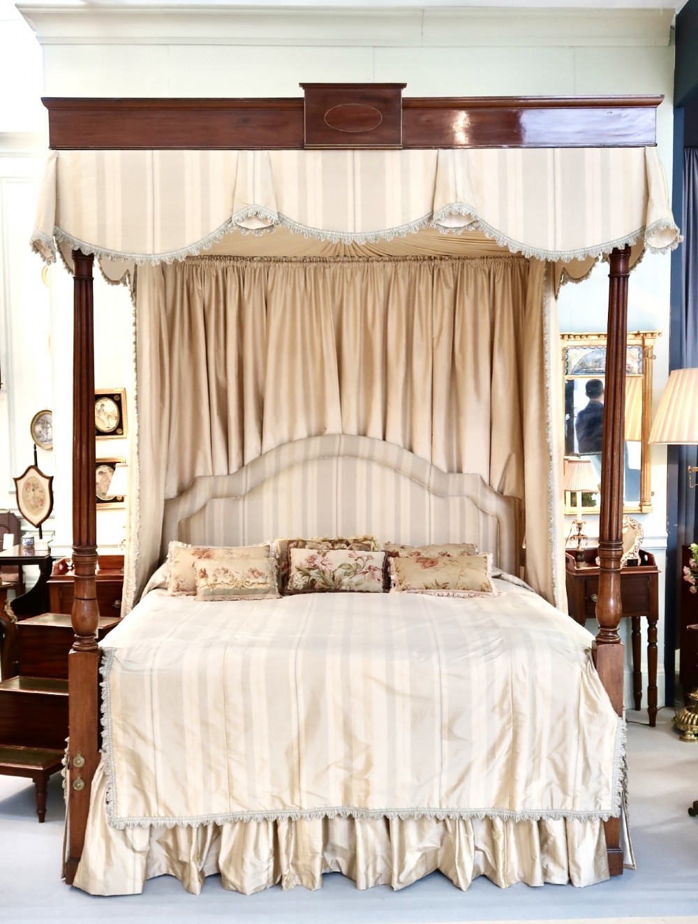 A large mahogany George III style super king four poster bed featuring turned posts, an inlaid wooden cornice, and cream striped fabric hangings.