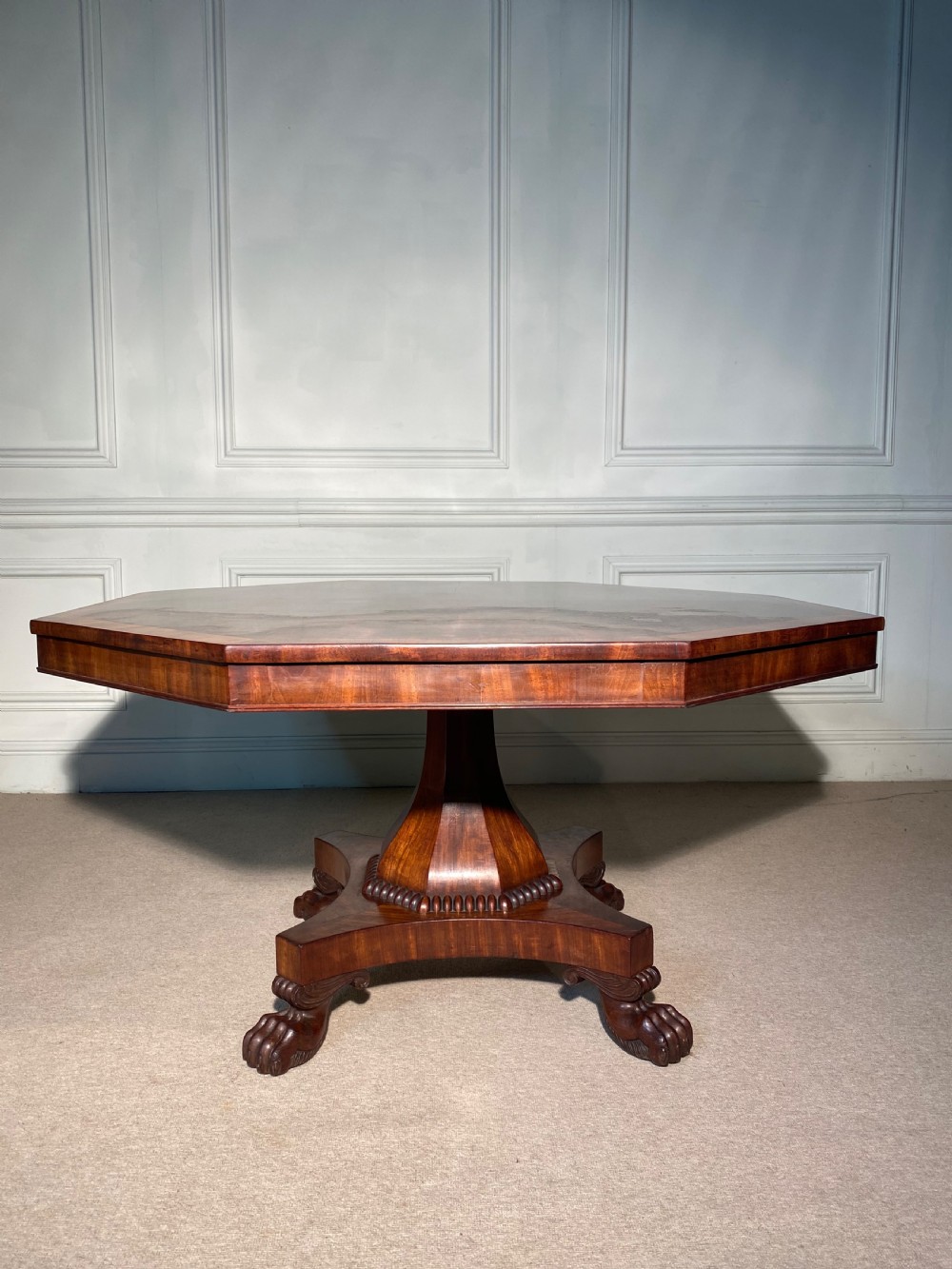 A Regency mahogany hexagonal centre table with a faceted pedestal support and carved lion paw feet.
