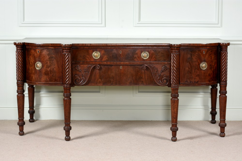 An antique Regency flame mahogany sideboard featuring spiral-turned legs, carved spandrels, multiple drawers, and brass ring handles.