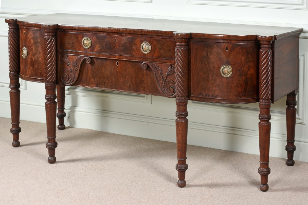 An antique Regency flame mahogany sideboard featuring spiral-turned legs, carved spandrels, multiple drawers, and brass ring handles. View II