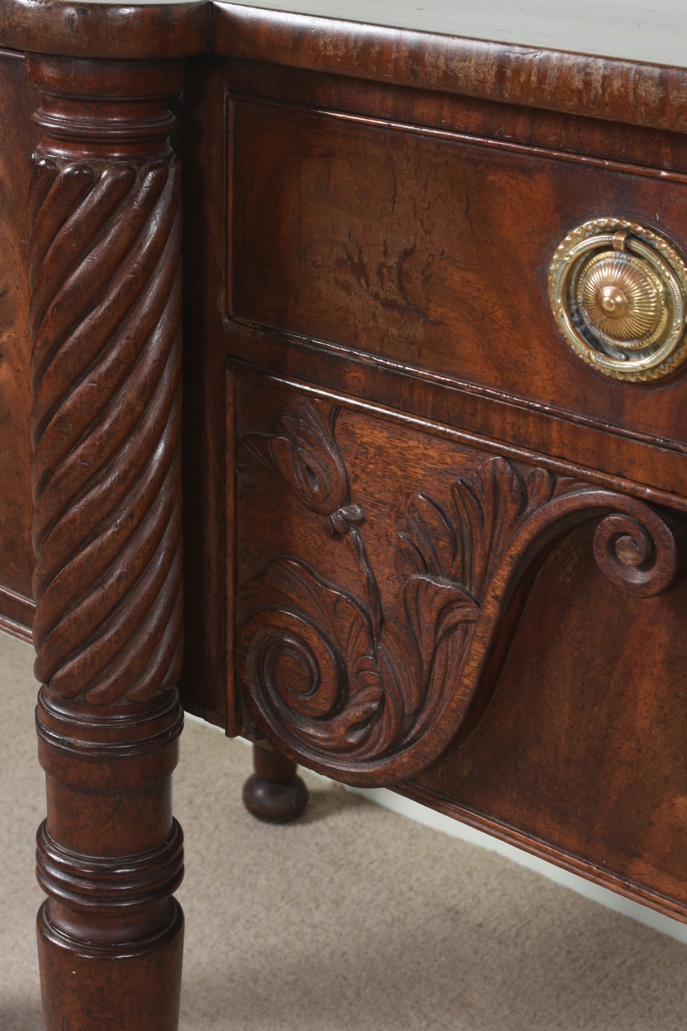 An antique Regency flame mahogany sideboard featuring spiral-turned legs, carved spandrels, multiple drawers, and brass ring handles. View V