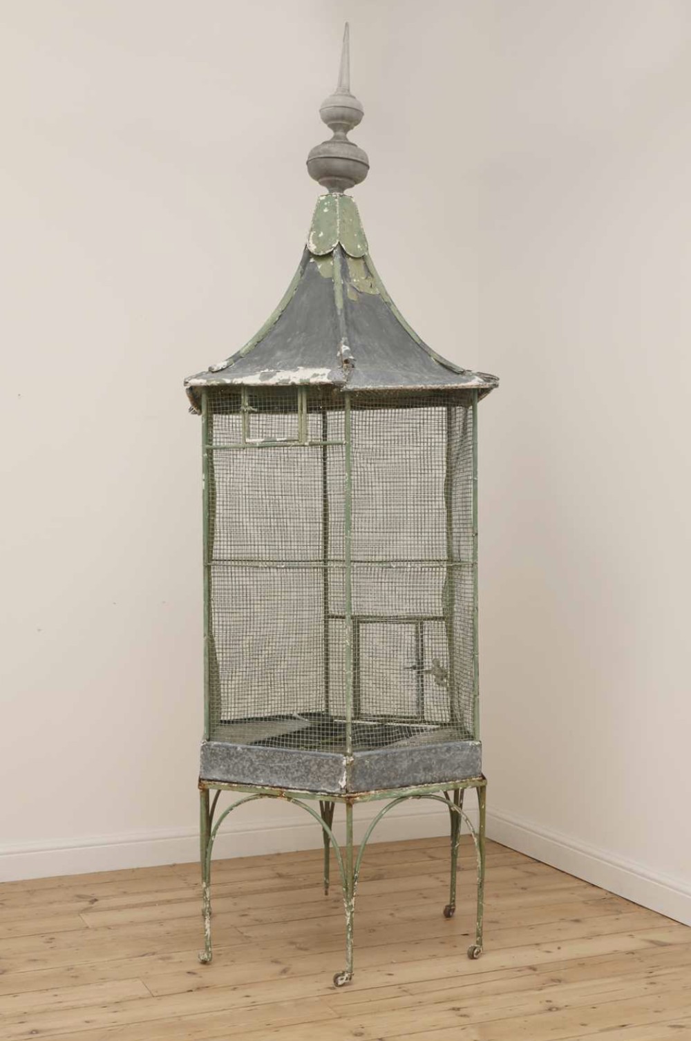 A tall 19th-century French standing zinc and wire mesh birdcage with a distressed green painted finish, pagoda turret roof, metal finial, and wheeled iron legs.