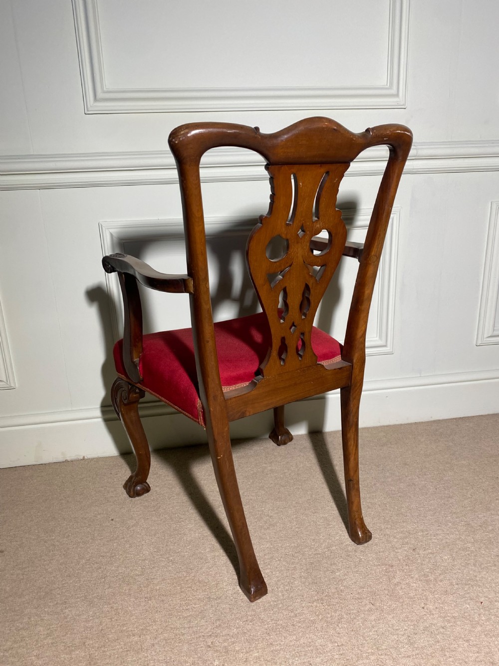 A Chippendale style carved mahogany carver chair featuring a pierced splat back, shaped scroll arms, red velvet seat cushion, and cabriole legs with ball and claw feet. View V