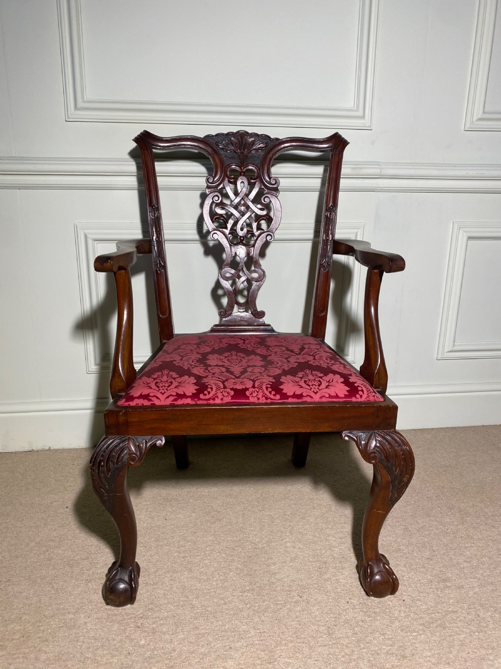 A Chippendale style mahogany carver armchair featuring an intricately carved pierced splat back, red patterned damask upholstery, and cabriole legs with ball and claw feet. View II