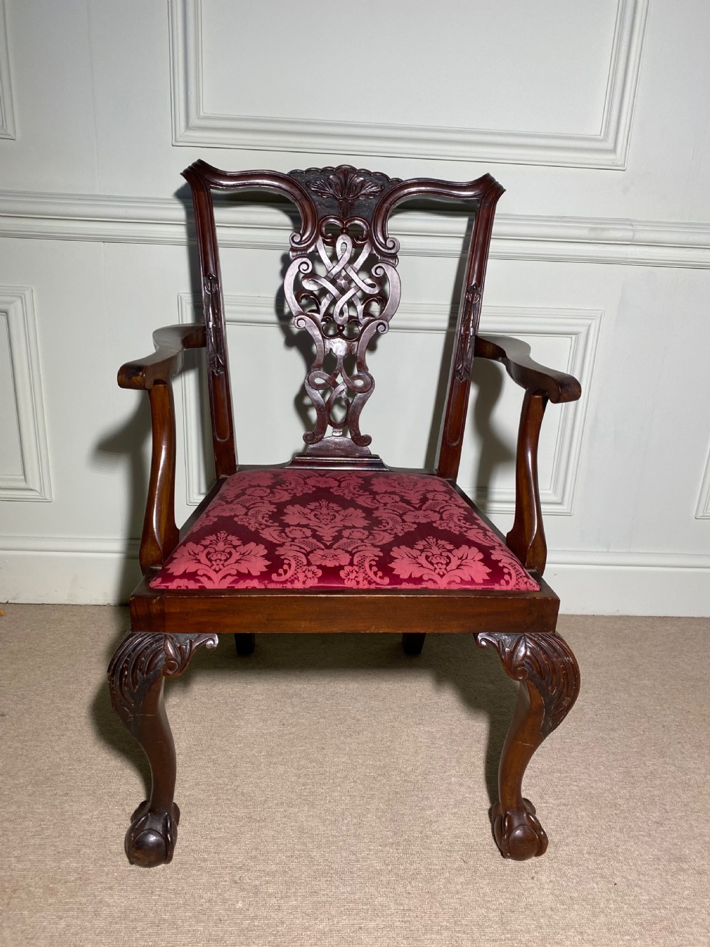 A Chippendale style mahogany carver armchair featuring an intricately carved pierced splat back, red patterned damask upholstery, and cabriole legs with ball and claw feet. View V