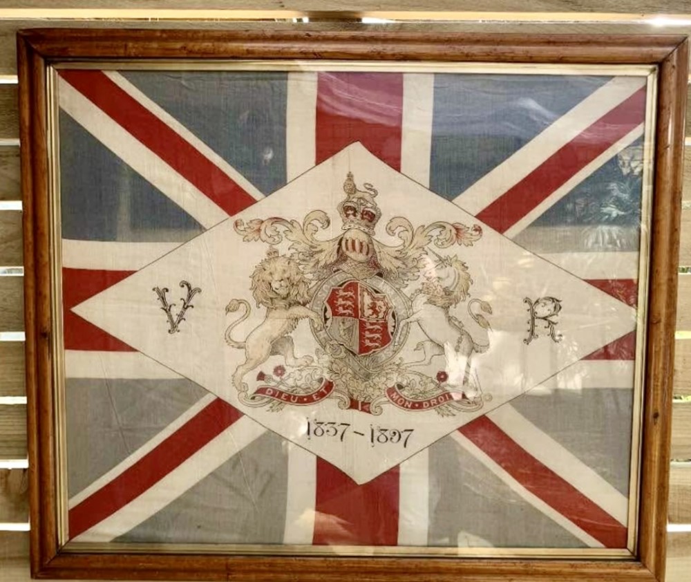 A framed 1897 Queen Victoria Diamond Jubilee Union Jack flag featuring the Royal Coat of Arms, VR initials, and dates 1837-1897 inside a glazed wooden frame.