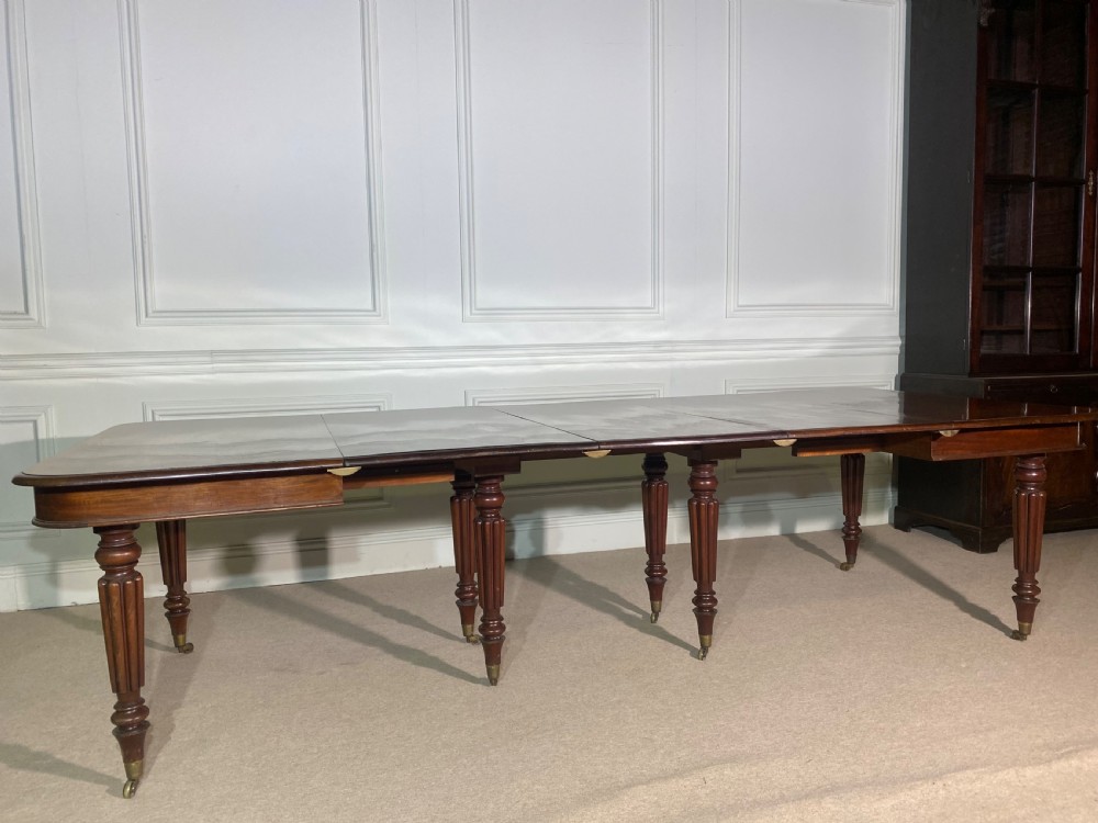 A large Regency mahogany extending dining table with insertable leaves, resting on turned reeded legs with brass castors. View II