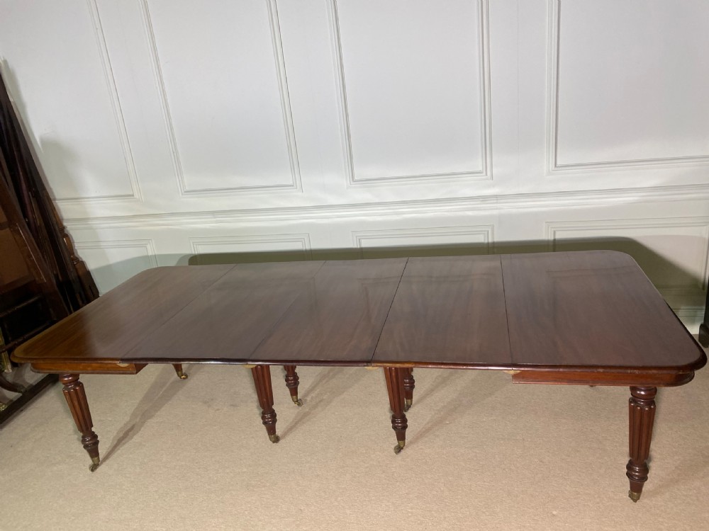 A large Regency mahogany extending dining table with insertable leaves, resting on turned reeded legs with brass castors. View III