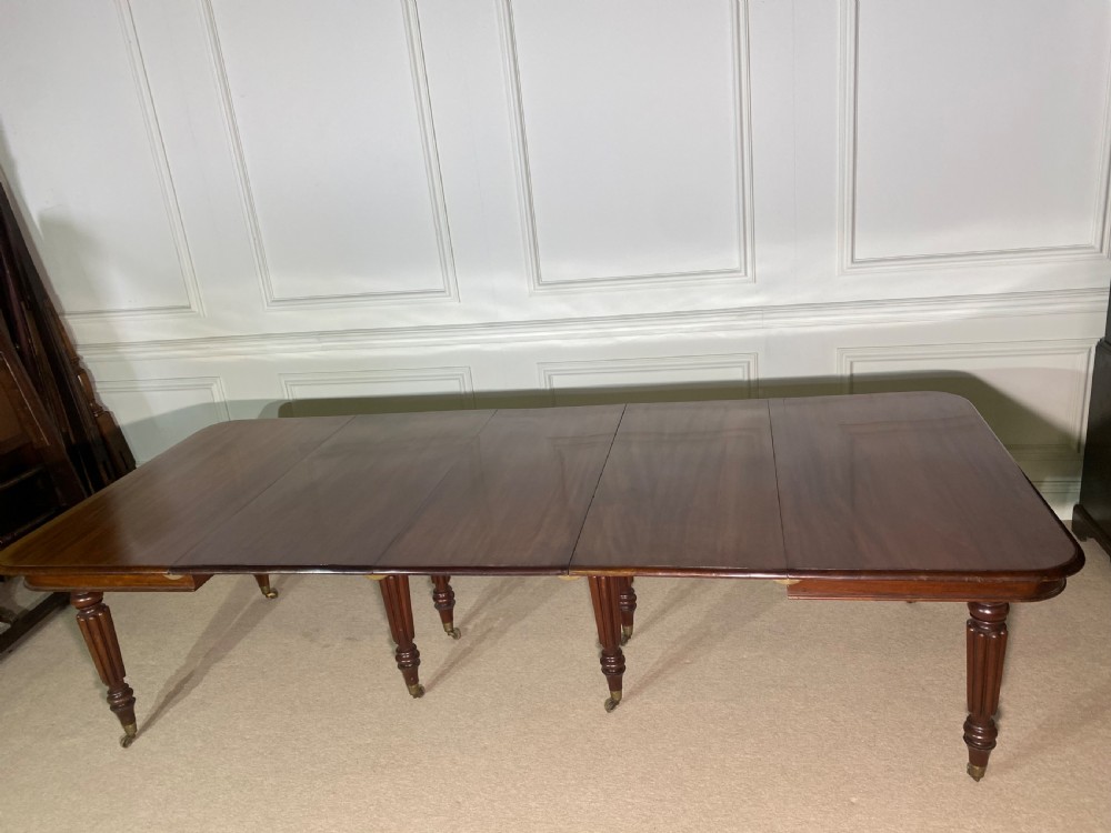 A large Regency mahogany extending dining table with insertable leaves, resting on turned reeded legs with brass castors. View IV