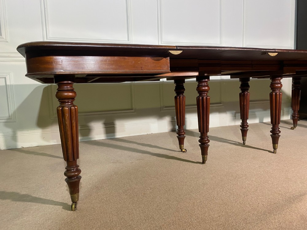 A large Regency mahogany extending dining table with insertable leaves, resting on turned reeded legs with brass castors. View IX