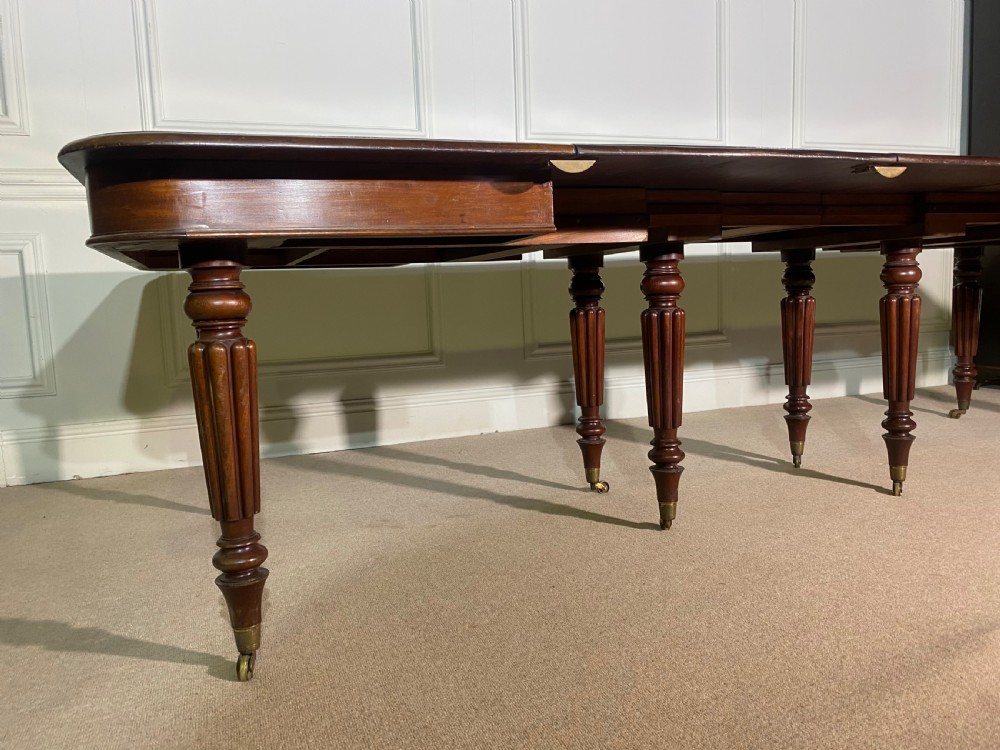 A large Regency mahogany extending dining table with insertable leaves, resting on turned reeded legs with brass castors. View X