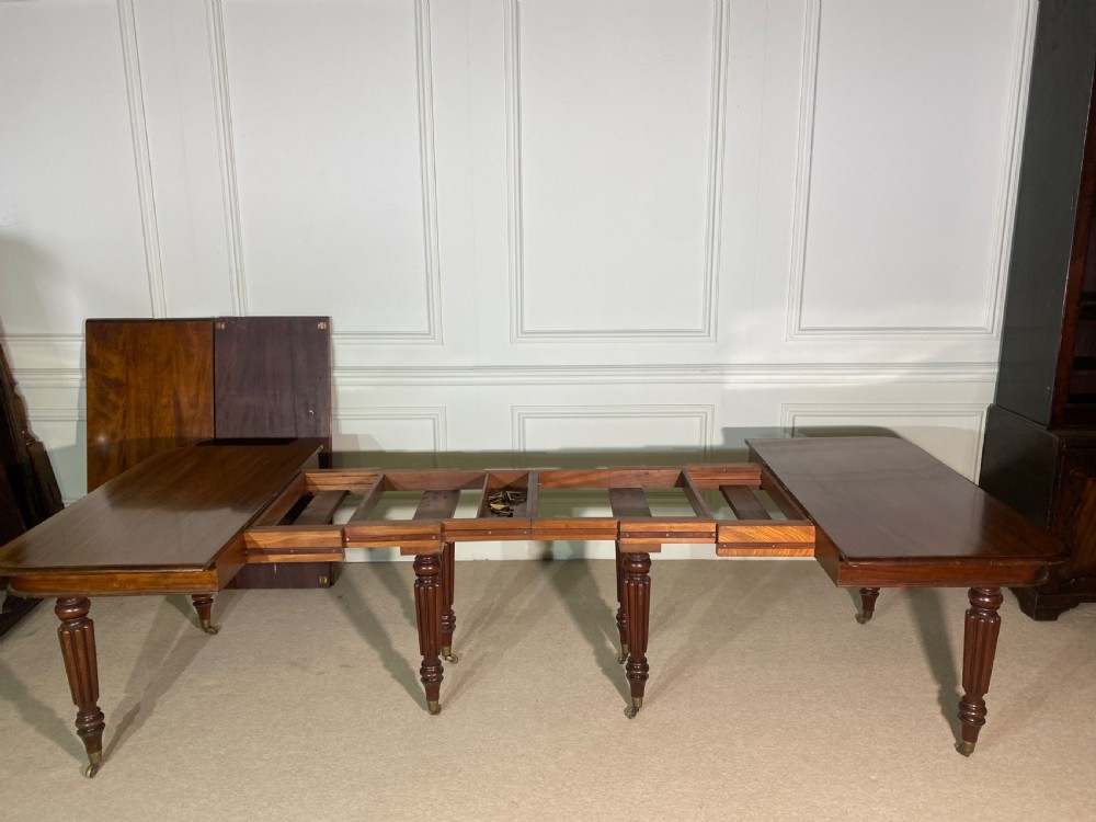 A large Regency mahogany extending dining table with insertable leaves, resting on turned reeded legs with brass castors. View XI