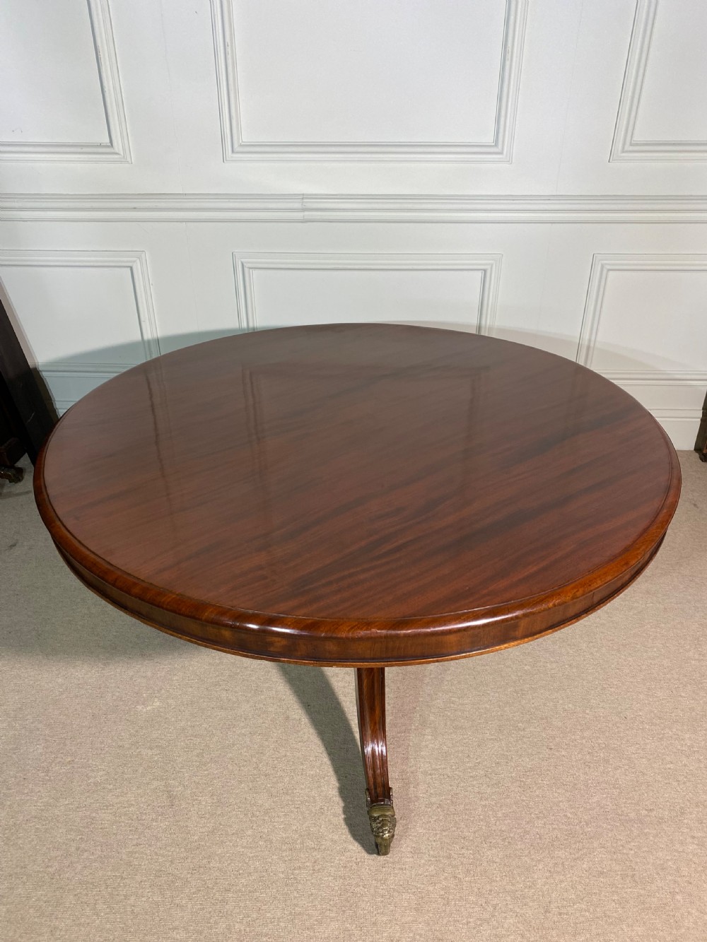 A circular Regency mahogany centre table featuring a polished top supported by a central column and splayed legs ending in brass lion paw castors.