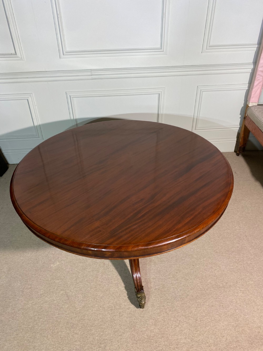 A circular Regency mahogany centre table featuring a polished top supported by a central column and splayed legs ending in brass lion paw castors. View II