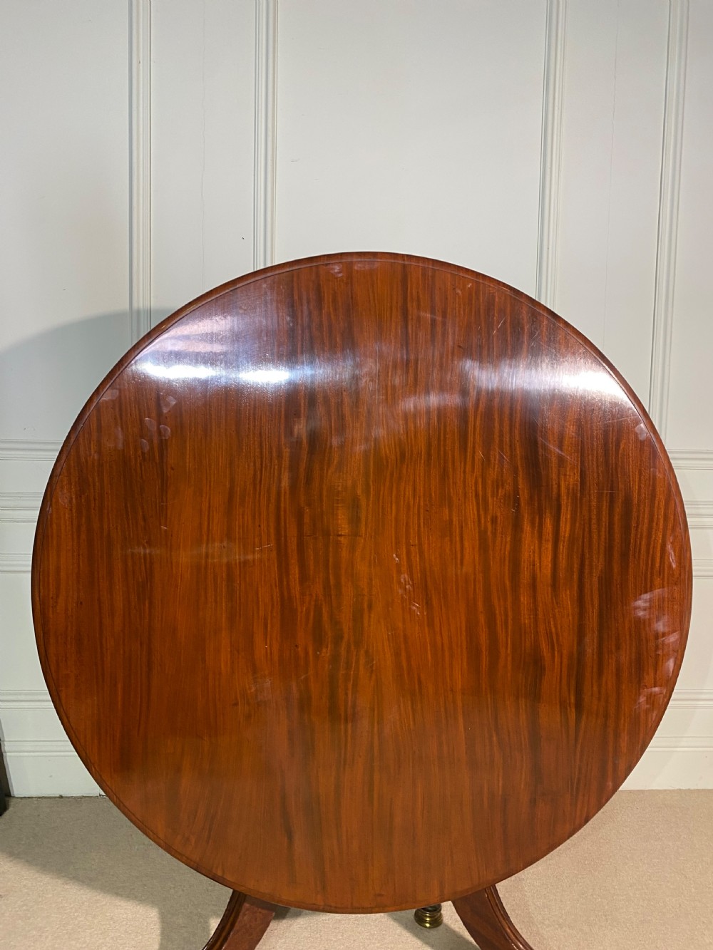 A circular Regency mahogany centre table featuring a polished top supported by a central column and splayed legs ending in brass lion paw castors. View III