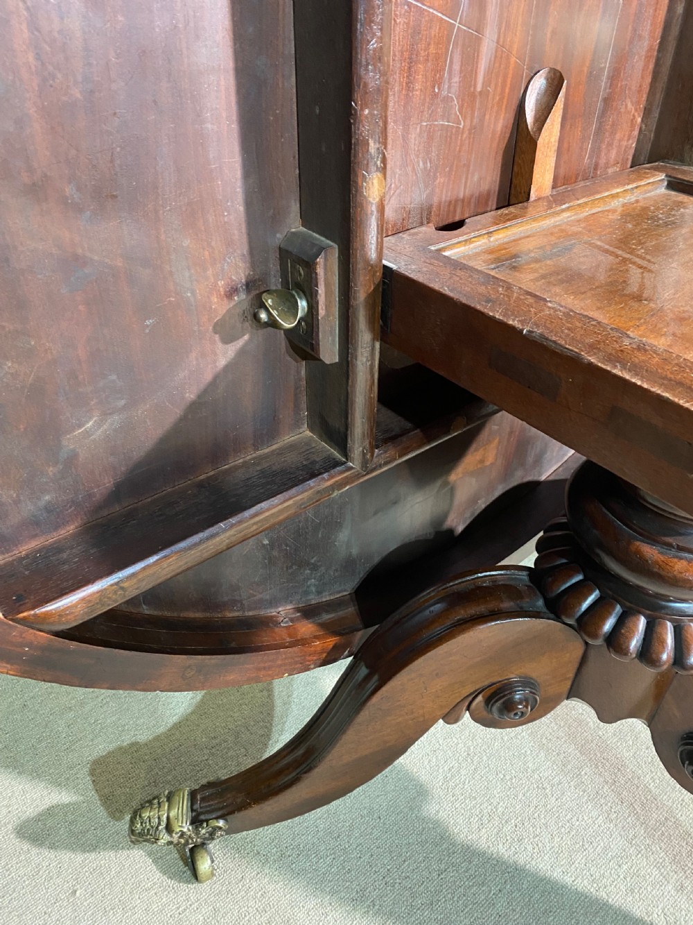 A circular Regency mahogany centre table featuring a polished top supported by a central column and splayed legs ending in brass lion paw castors. View IV