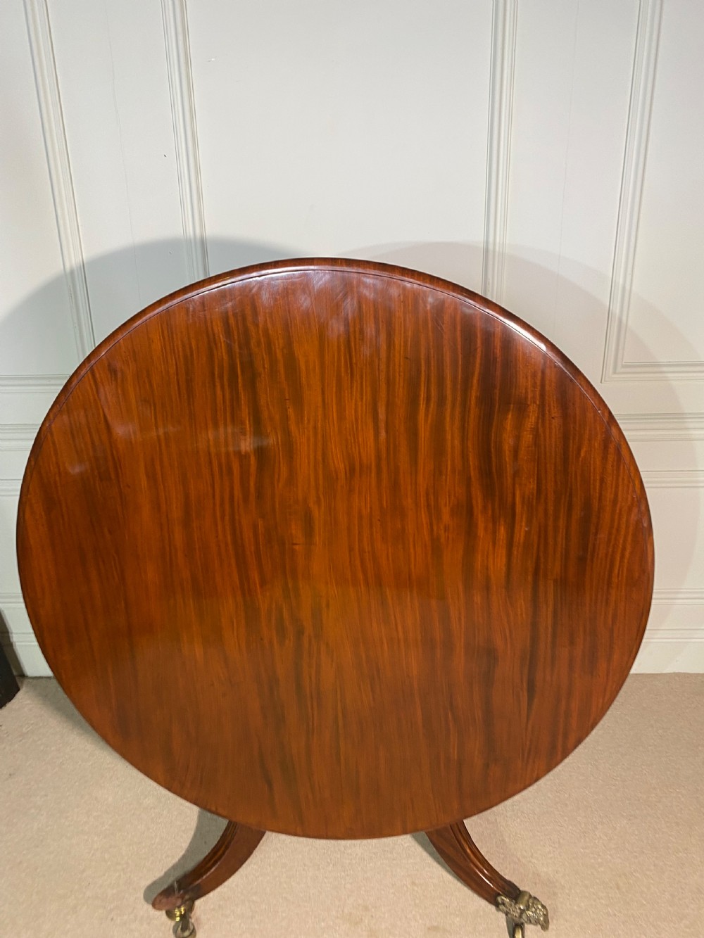 A circular Regency mahogany centre table featuring a polished top supported by a central column and splayed legs ending in brass lion paw castors. View VI