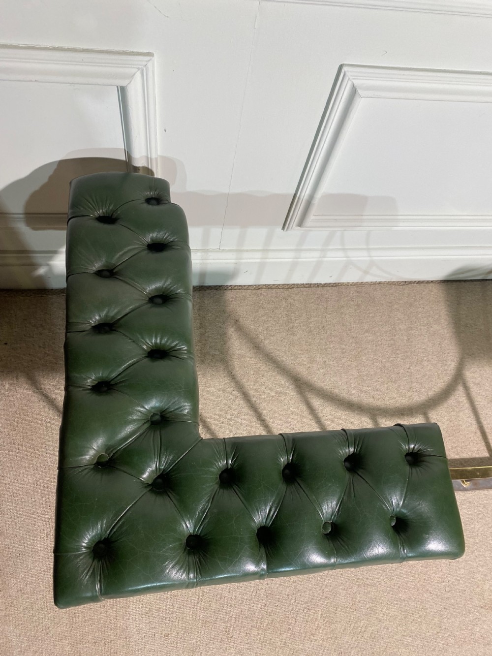 A metal fireplace club fender with vertical steel uprights, brass accents, a central curved dip, and two corner seats upholstered in button-tufted dark green leather with brass studding. View V
