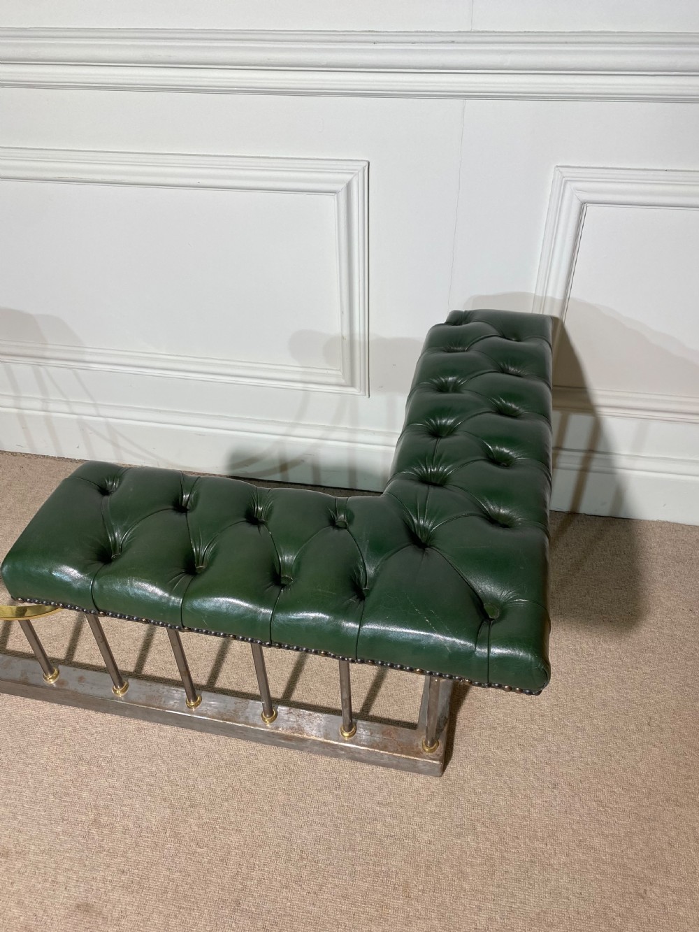 A metal fireplace club fender with vertical steel uprights, brass accents, a central curved dip, and two corner seats upholstered in button-tufted dark green leather with brass studding. View VI