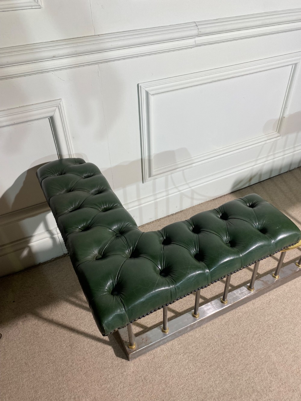A metal fireplace club fender with vertical steel uprights, brass accents, a central curved dip, and two corner seats upholstered in button-tufted dark green leather with brass studding. View VIII
