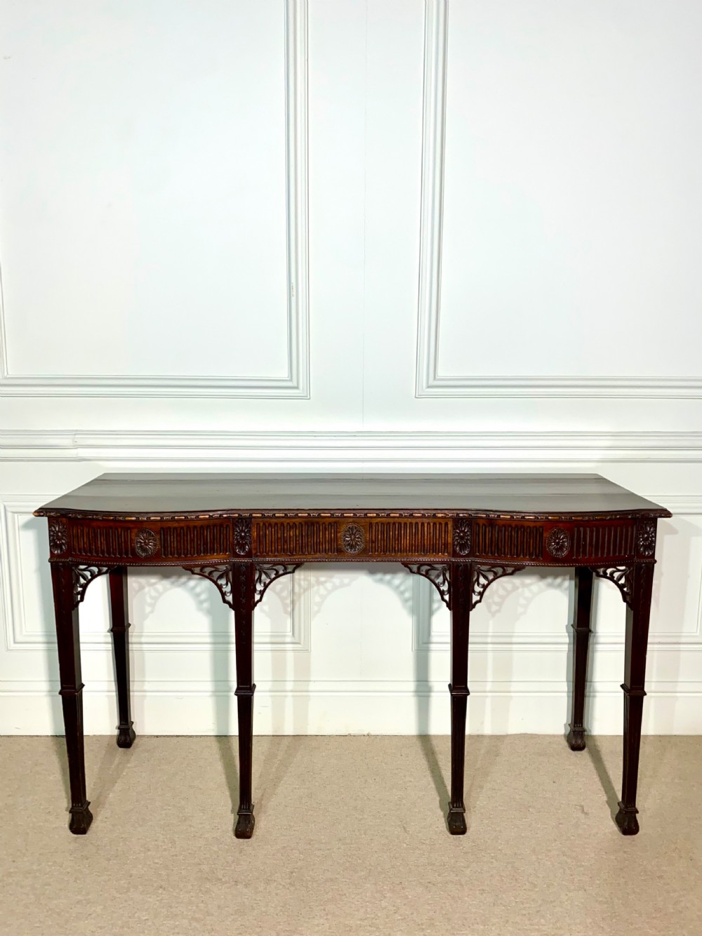 A narrow dark mahogany console table in the Neoclassical style featuring carved patera rosettes, a fluted frieze, corner spandrel brackets, and four square tapered legs.