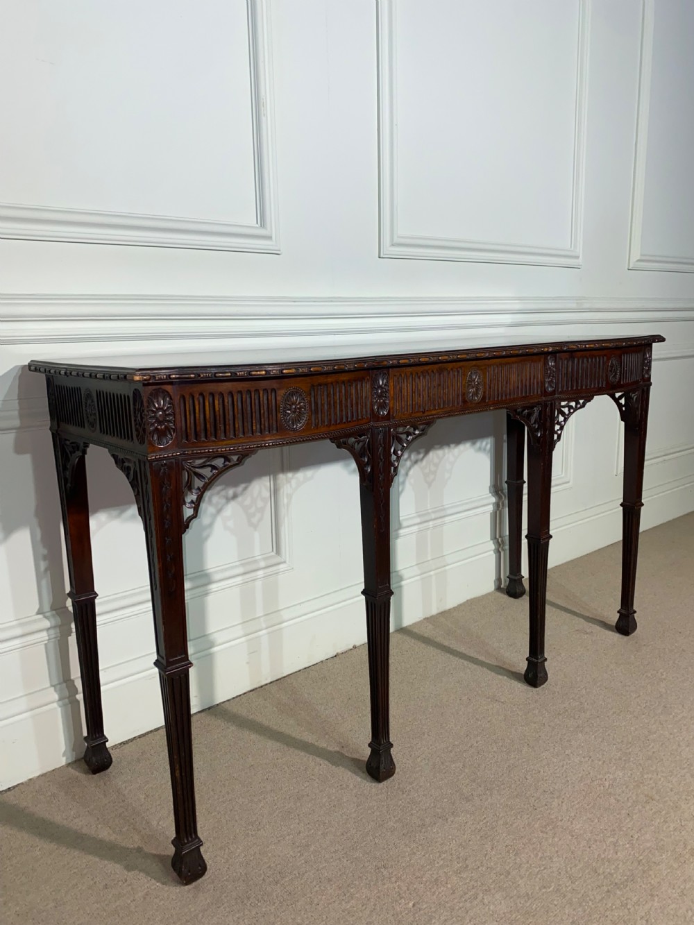 A narrow dark mahogany console table in the Neoclassical style featuring carved patera rosettes, a fluted frieze, corner spandrel brackets, and four square tapered legs. View II