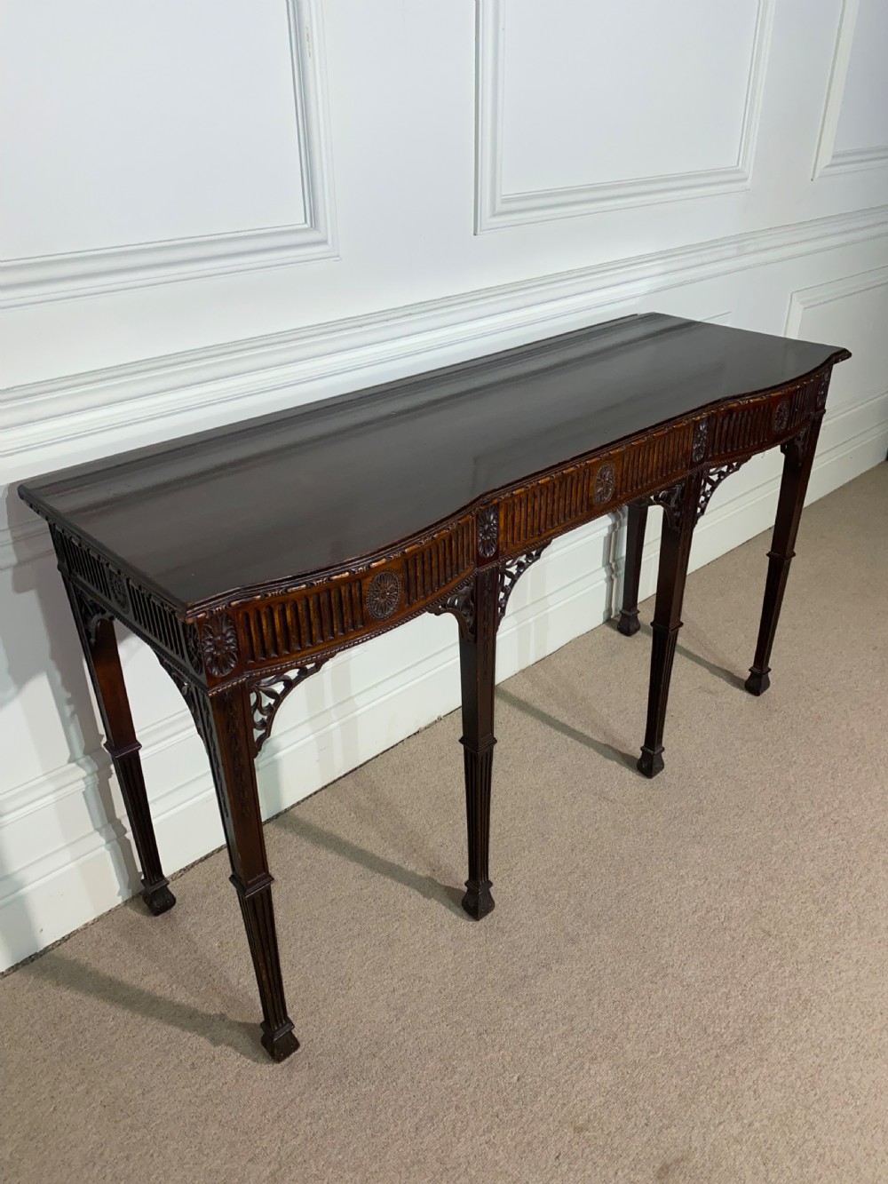 A narrow dark mahogany console table in the Neoclassical style featuring carved patera rosettes, a fluted frieze, corner spandrel brackets, and four square tapered legs. View III