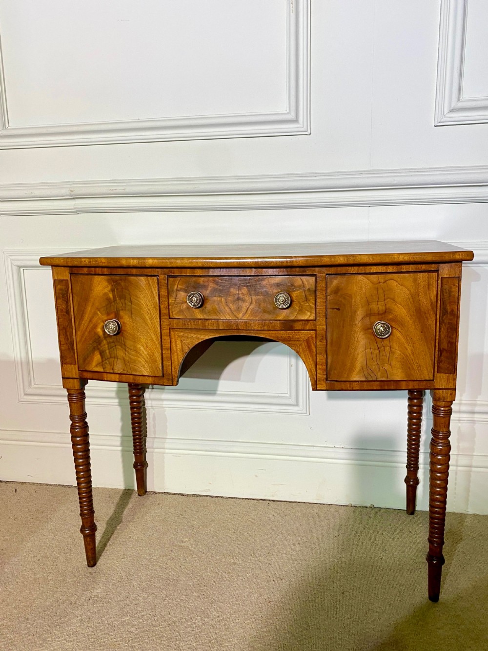 A George III bow-fronted mahogany dressing table featuring three drawers with round brass knobs, an arched central kneehole, and four turned legs. View II
